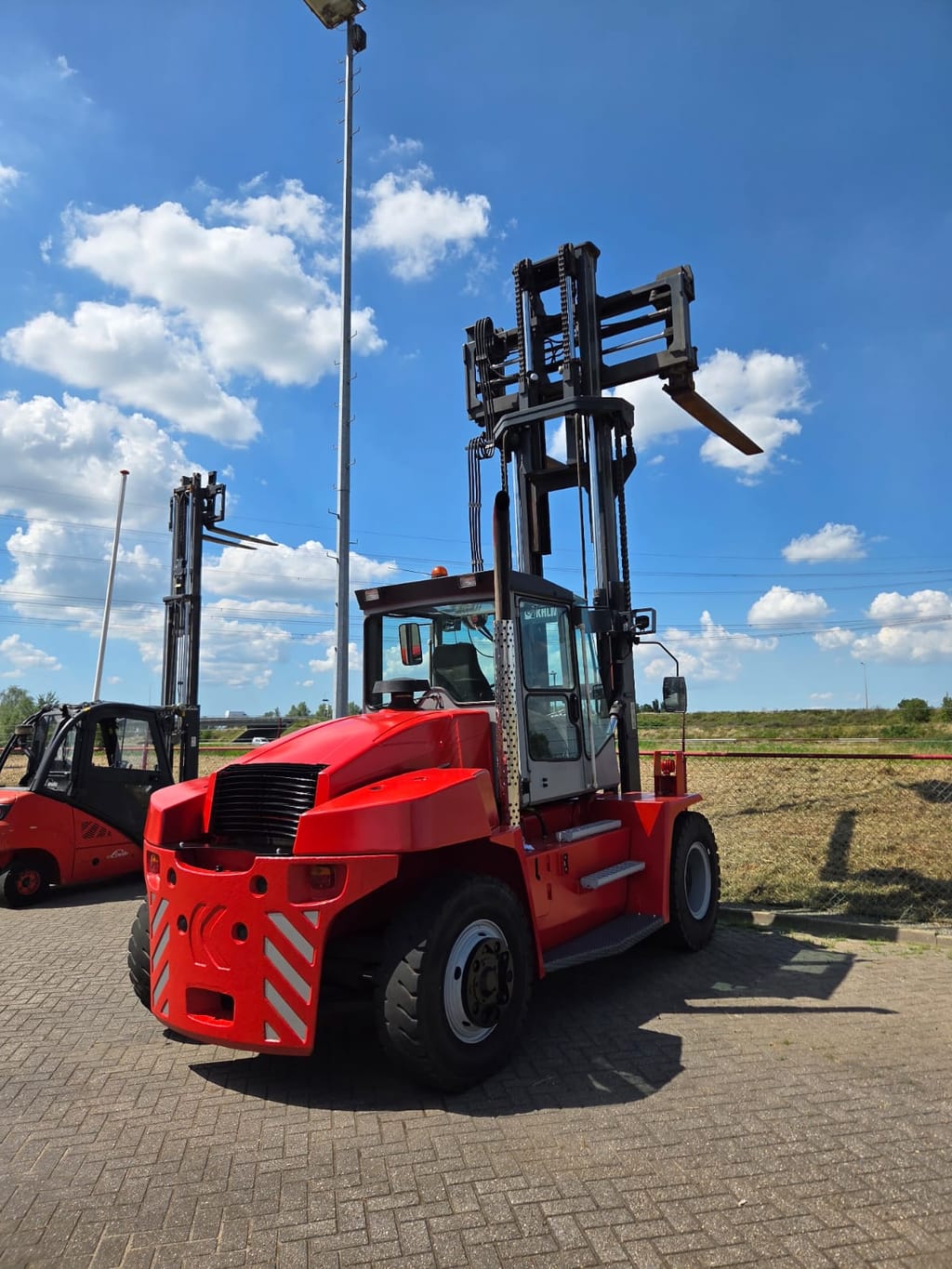 Een grote rode zware heftruck op het terrein van BM in Dodewaard, met een Linde heftruck op de achtergrond