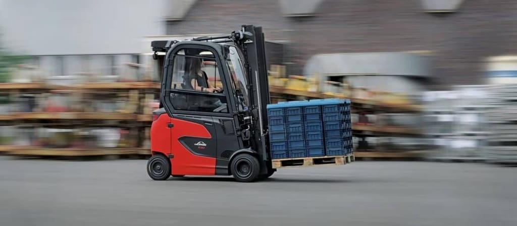 Een rijdende Linde elektrische heftruck met een pallet blauwe kratten op een buitenterrein