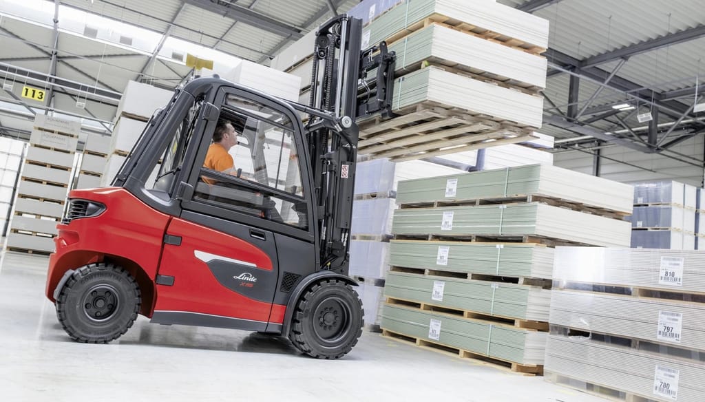 Een chauffeur op een Linde heftruck tilt een pallet met gipsplaten hoog in een magazijn